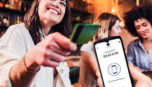 Eine Frau in einer Gastwirtschaft freut sich darüber, dass sie mit einer Karte bezahlen kann, die sie an ein mobiles Kassenendgerät hält.